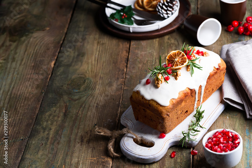 Cuadro en lienzo Fruit cake dusted with icing, nuts, kernels pomegranate and dry orange on old wooden background