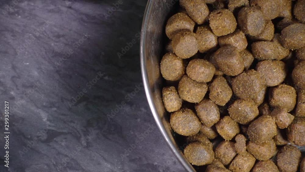 Slow motion close POV overhead shot of a man’s hands cutting a piece of moist dog chub meat roll and adding it to a large steel bowl containing dry biscuit / kibble. Slow motion close POV overhead shot of a man’s hands cutting a piece of moist dog chub meat roll and adding it to a large steel bowl containing dry biscuit / kibble.