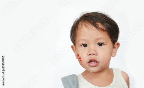Portrait of little Asian baby boy with face make up sticker lesion on face in Halloween costume looking camera over white background.
