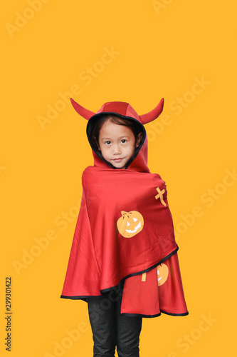Peaceful little Asian child girl dressed Halloween costume. Kid in Dracula robe isolated on orange background.