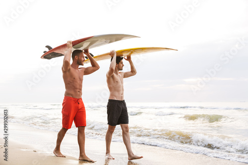 Two men surfers friends with surfings on a beach outside.