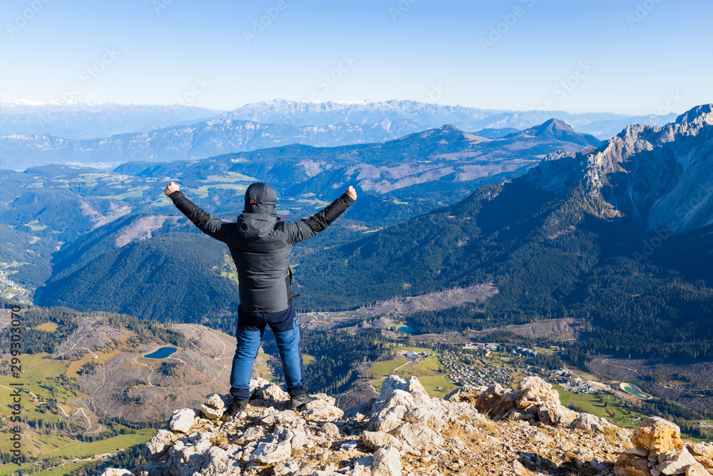 A happy man stands on a mountain and looks at the Alpine valley