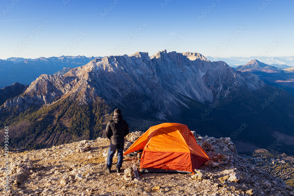 A man with a tent on top of the mountain meets the morning. The beautiful Italian Alps