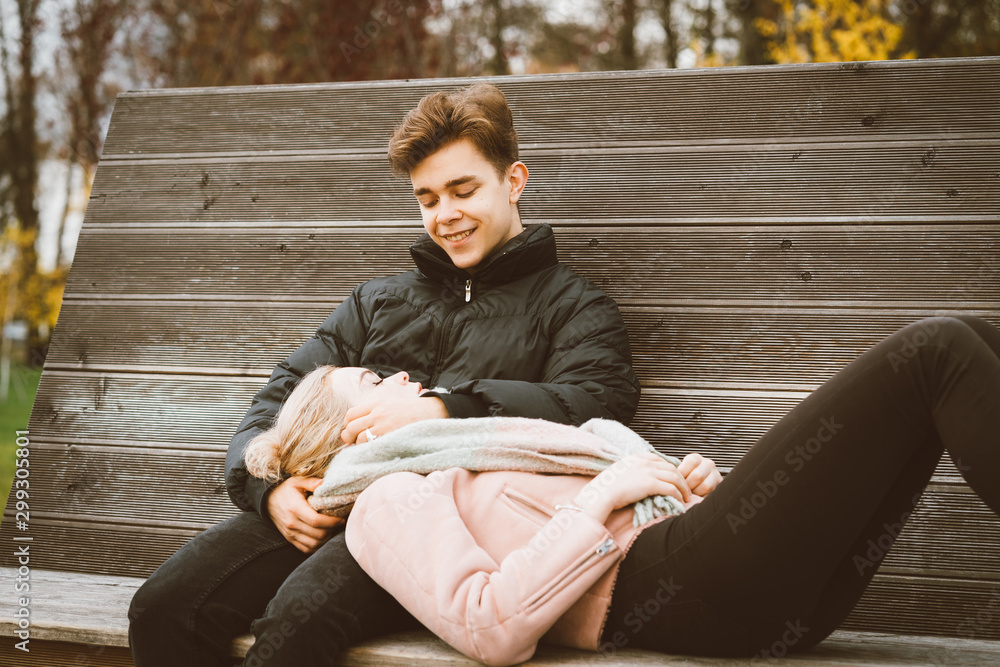 Teenagers in love are sitting on park bench in autumn, chatting cheerfully,  talking. Cute blonde girl lies, her head on boy lap, guy smiles. Teenage  love concept. Stock Photo | Adobe Stock