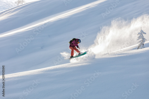 freerider in a bright suit rides fast skiing with large splashes of snow on a sunny day. Young Beautiful female skier. Snow scoot. Extreme winter sports. sunrise light, edit space. 