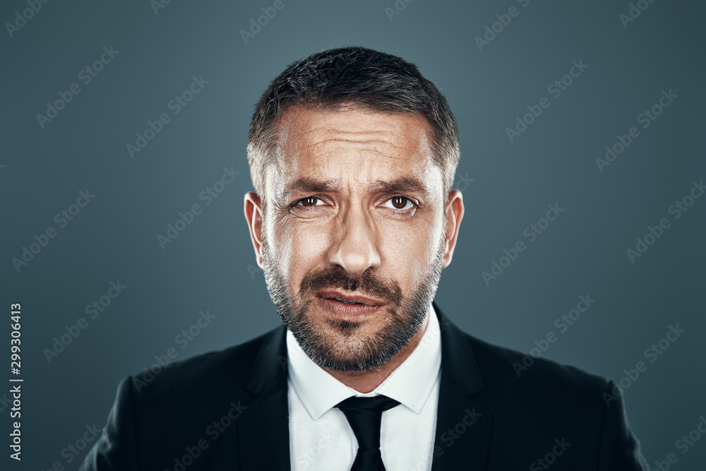 Charming young man in full suit looking at camera while standing against grey background Charming young man in full suit looking at camera while standing against grey background
