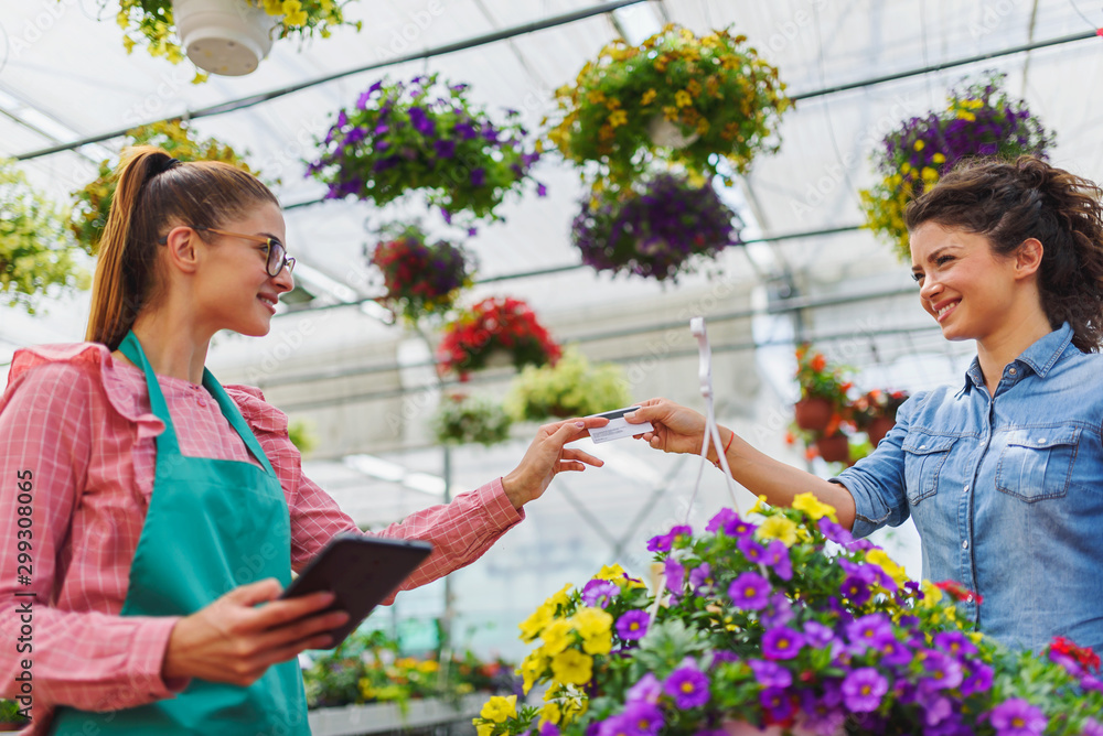 Young woman buying flowers with credit card in greenhouse Young woman buying flowers with credit card in greenhouse
