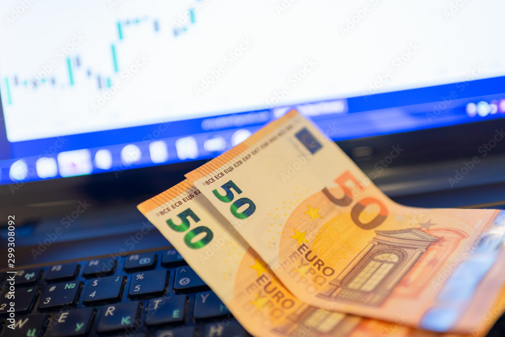 Two fifty euro banknotes on a laptop keyboard. with diagrams on the stock market. Two fifty euro banknotes on a laptop keyboard. with diagrams on the stock market.