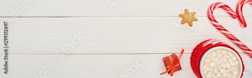 top view of christmas candy canes, little gift and cup of cocoa with marshmallows on white wooden table