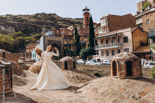 01.06.2019 Tbilisi, Georgia: beautiful young girl in exquisite wedding dress posing for photo on roof of Georgian sulfur baths on old city background