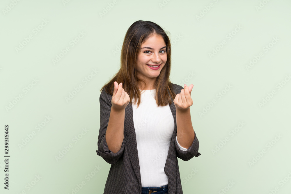 Young brunette girl with blazer over isolated green background making money gesture Young brunette girl with blazer over isolated green background making money gesture
