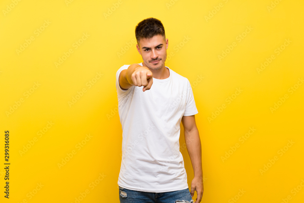 Young handsome man over isolated yellow background points finger at you with a confident expression Young handsome man over isolated yellow background points finger at you with a confident expression