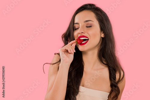 happy woman with red lips eating strawberry isolated on pink