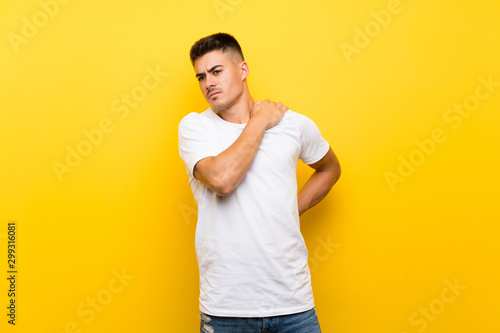 Young handsome man over isolated yellow background suffering from pain in shoulder for having made an effort