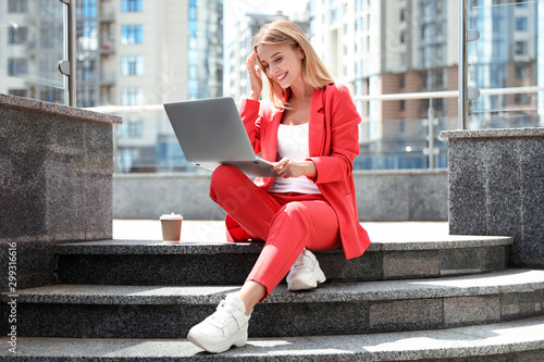 Beautiful businesswoman with laptop sitting on stairs outdoors photo