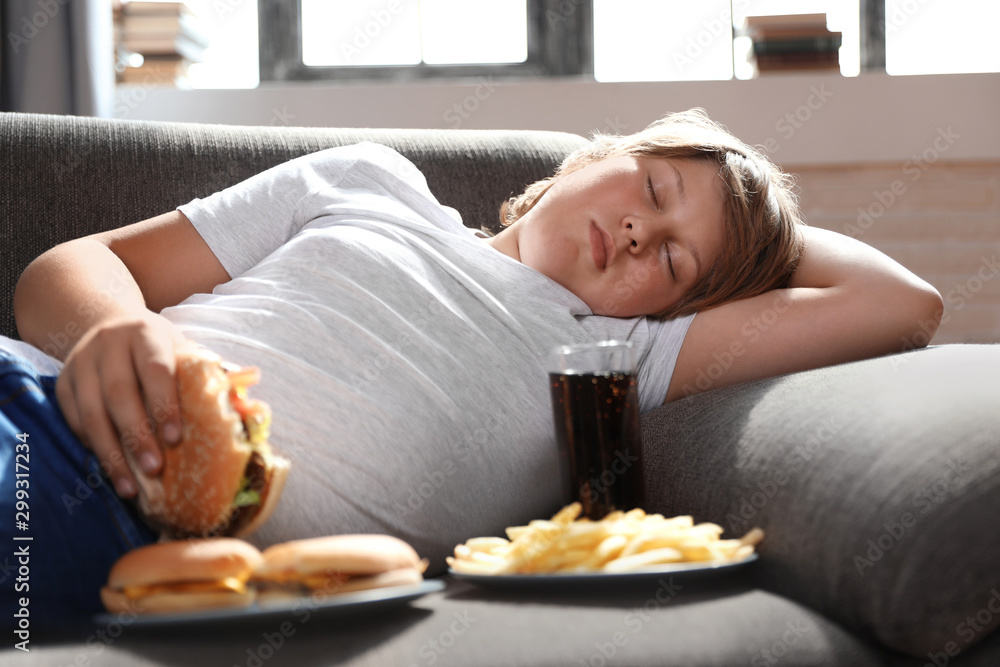 Overweight boy sleeping on sofa surrounded by fast food