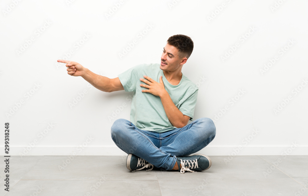 Young handsome man sitting on the floor pointing finger to the side Young handsome man sitting on the floor pointing finger to the side