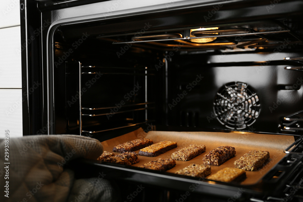 Woman taking delicious healthy granola bars from oven, closeup - obrazy, fototapety, plakaty 
