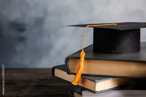 Graduation hat, books and student's diploma on wooden table against light blue background