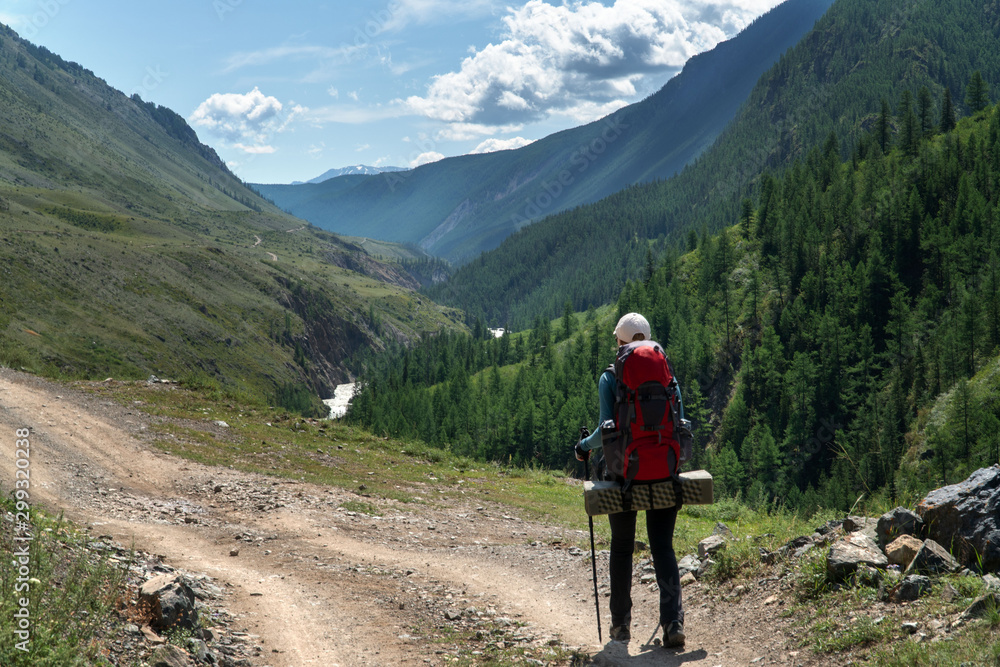 A girl with a backpack walks along a trail along a mountain river. Background for outdoor travel.