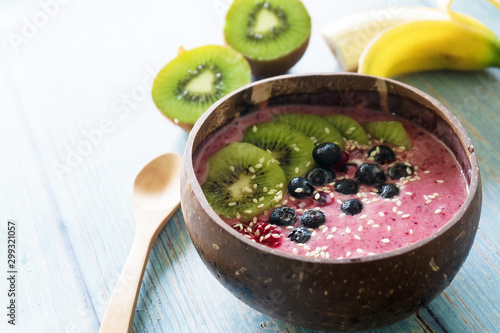 Bowl with yummy berry smoothie on blue wooden table. Healthy vegan food concept.