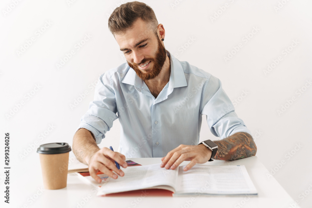 Image of brunette man sitting at table and studying with exercise books Image of brunette man sitting at table and studying with exercise books