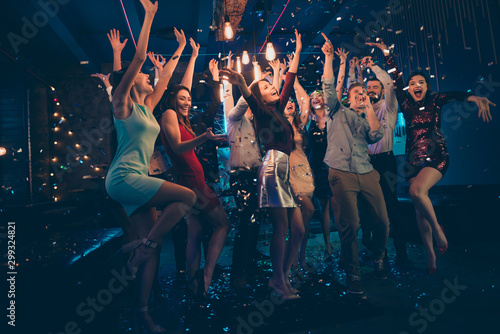 Full length body size photo of company dancing cheerfully at night club under falling confetti and light of shining lamps with smiles on their faces