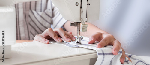 Obraz na plátne Hands of a girl sews on a white sewing machine close-up on a blue background wit