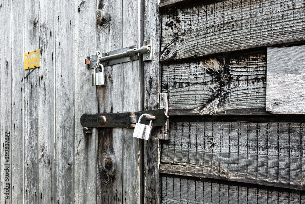 Monochrome view of a wooden, locked garden shed. The rough grain texture of the wooden panels is evident in the image. The shed is locked. Monochrome view of a wooden, locked garden shed. The rough grain texture of the wooden panels is evident in the image. The shed is locked.