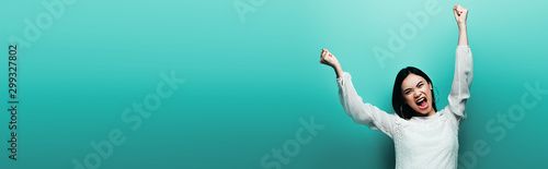 angry happy brunette asian woman yelling on turquoise background, panoramic shot