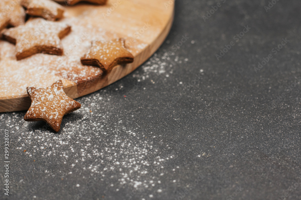 Star-shaped gingerbread cookie sprinkled with icing sugar on a wooden round cutting board.	