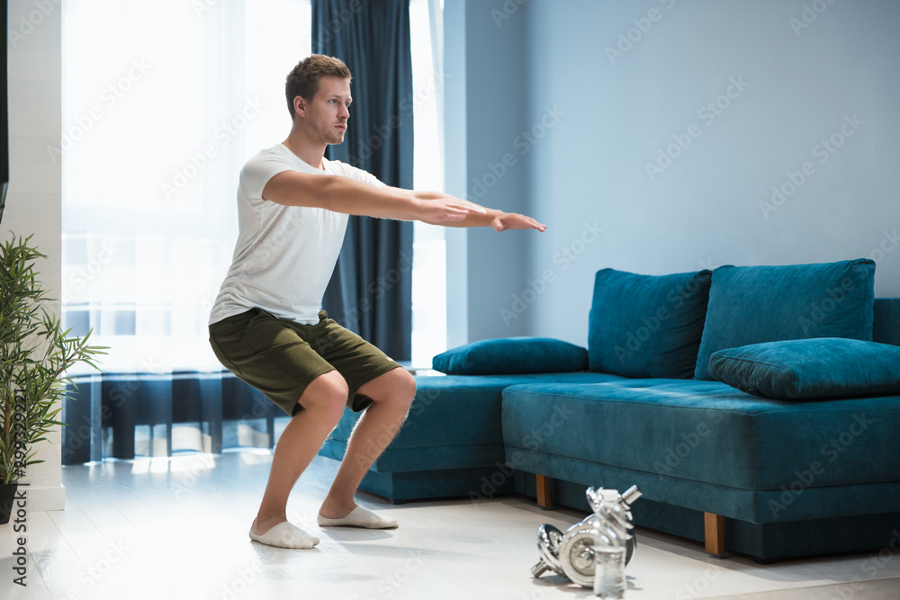 young handsome man doing squats during workout at home looking focused sporty and healthy lifestyle young handsome man doing squats during workout at home looking focused sporty and healthy lifestyle