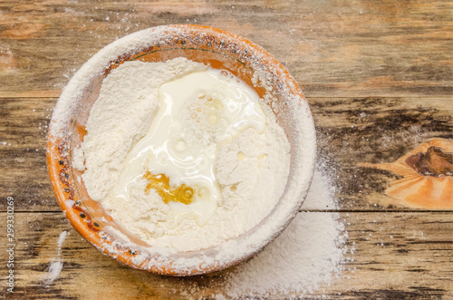 brown bowl with flour, egg and milk stands on a wooden background, top view, copy space