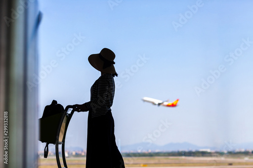 Tourist is standing in airport and looking at aircraft flight through window. 