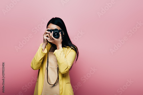 asian woman in yellow outfit taking picture on digital camera isolated on pink