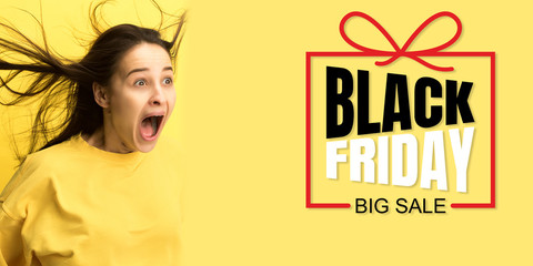 Portrait of young caucasian woman surprised and shocked of black friday on yellow background. Concept of sales, black friday, cyber monday, finance, business, purchases. Online shops and payments bill