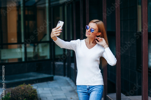 Portrait of a young attractive business woman making selfie photo on smartphone on a street background