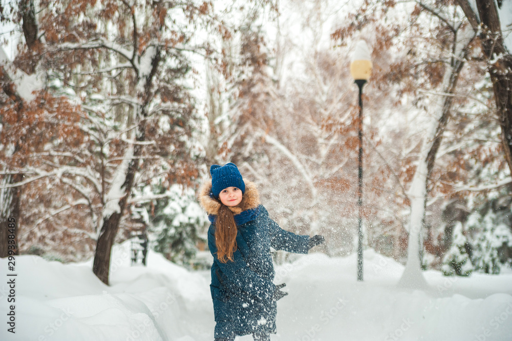 Naklejka premium Girl in the winter forest close-up and copy space. A child plays in the winter with snow.