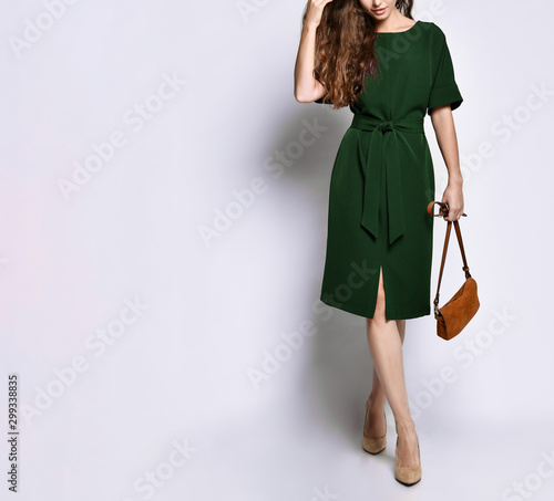 female legs in high-heeled shoes in a green dress from the designer and brown women's handbag on a white background photo