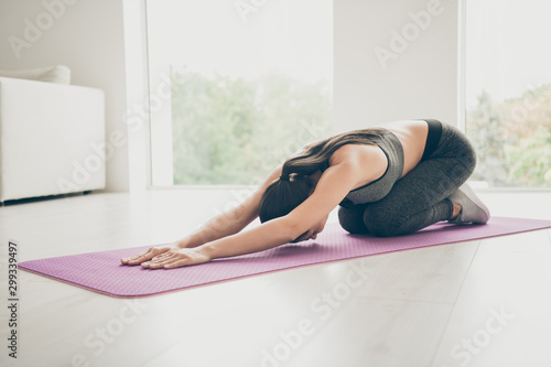 Full body photo of concentrated motivated girl sit on floor purple mat stretching her arms leaning want be strong physically fit woman wearing modern stylish pants clothes in gym like house photo