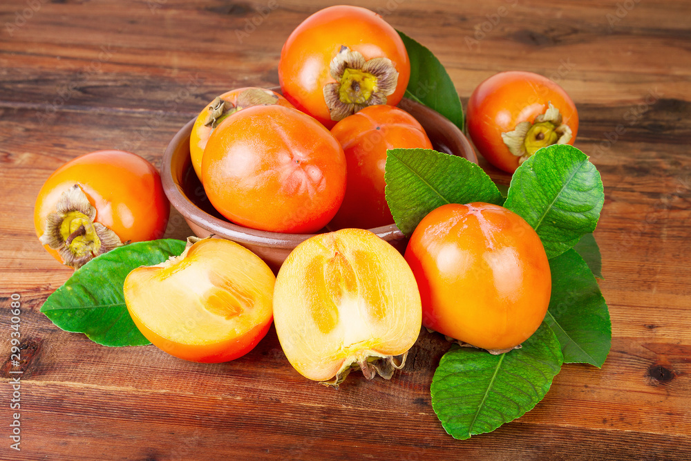 Persimmon or Kaki Fruit With Leaf In Bowl On Wooden Background Persimmon or Kaki Fruit With Leaf In Bowl On Wooden Background