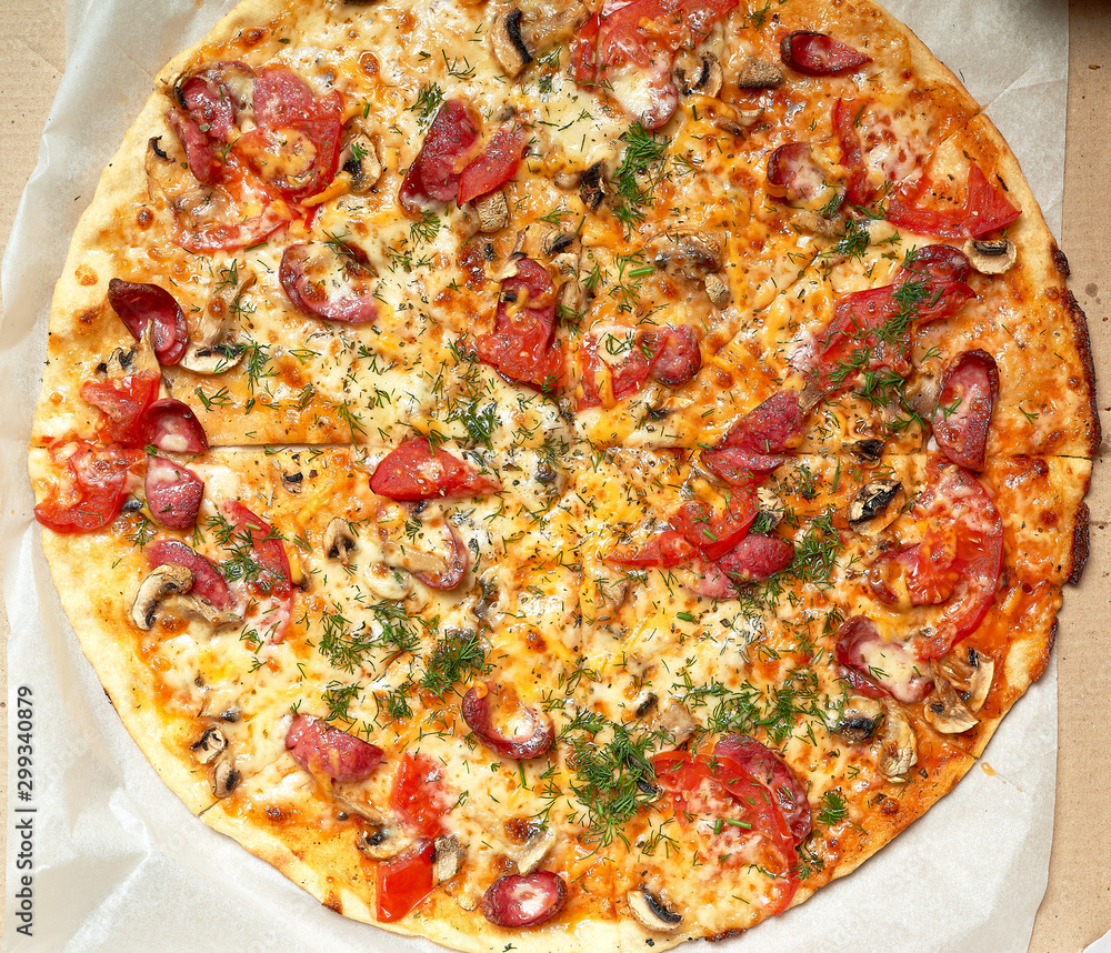 baked round pizza with smoked sausages, mushrooms, tomatoes, cheese and dill in an open cardboard box