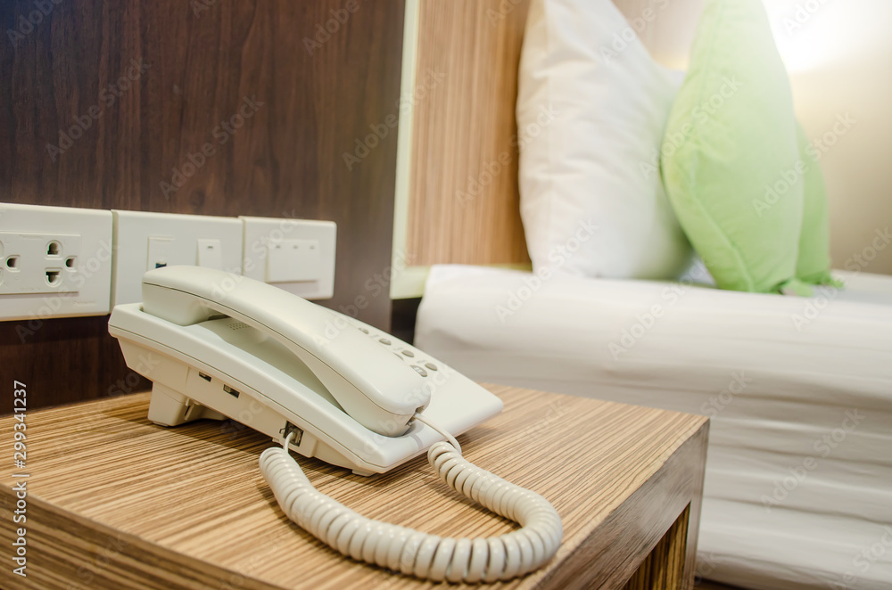 The white telephone on desk near a bed in hotel The white telephone on desk near a bed in hotel