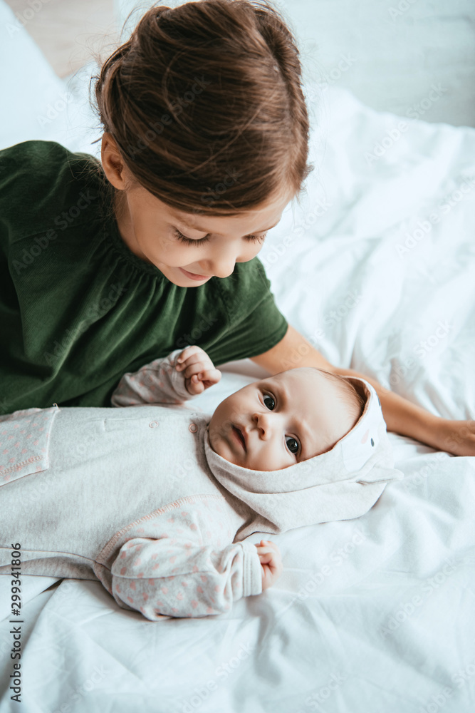 adorable child looking at cute little sister lying on white bedding adorable child looking at cute little sister lying on white bedding