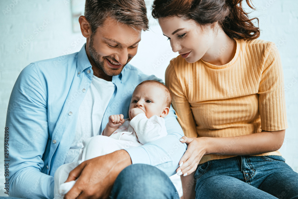 happy mother sitting near smiling husband holding cute little daughter