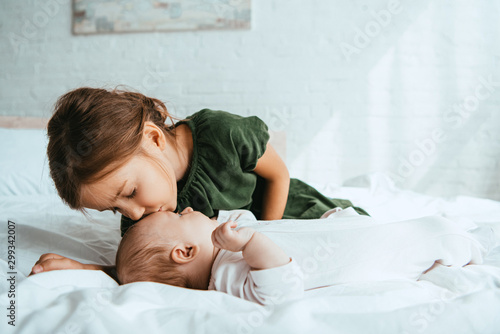 adorable child kissing little sister lying on white bedding photo