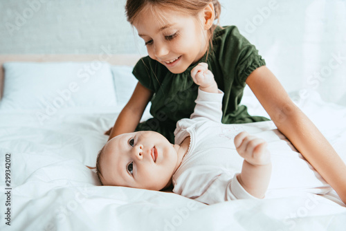 smiling child looking at adorable infant lying on white bedding