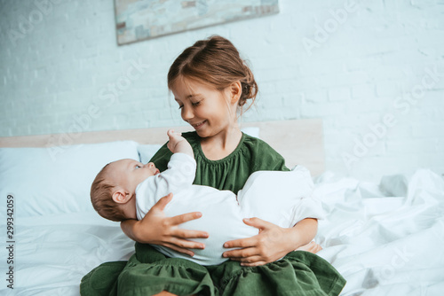 Schilderij op canvas happy child holding cute little sister while sitting on white bedding