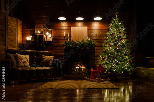 Christmas and New Year interior  fireplace  lamps  green Christmas tree  brown leather sofa  gifts  candles  moose rocking chair.  Lots of lights glowing in the dark.