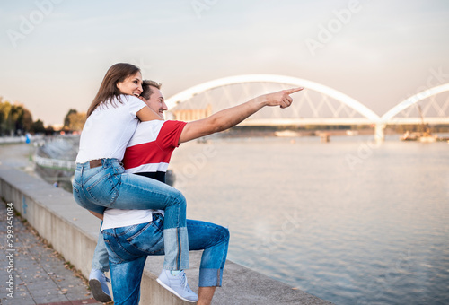 Outdoor shot of man giving woman piggyback on a riverbank
